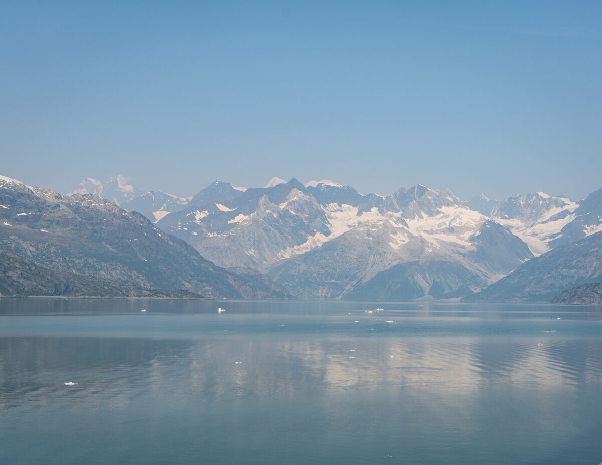 snow colored mountains reflected against the the bay with chunks of glaciers in the water