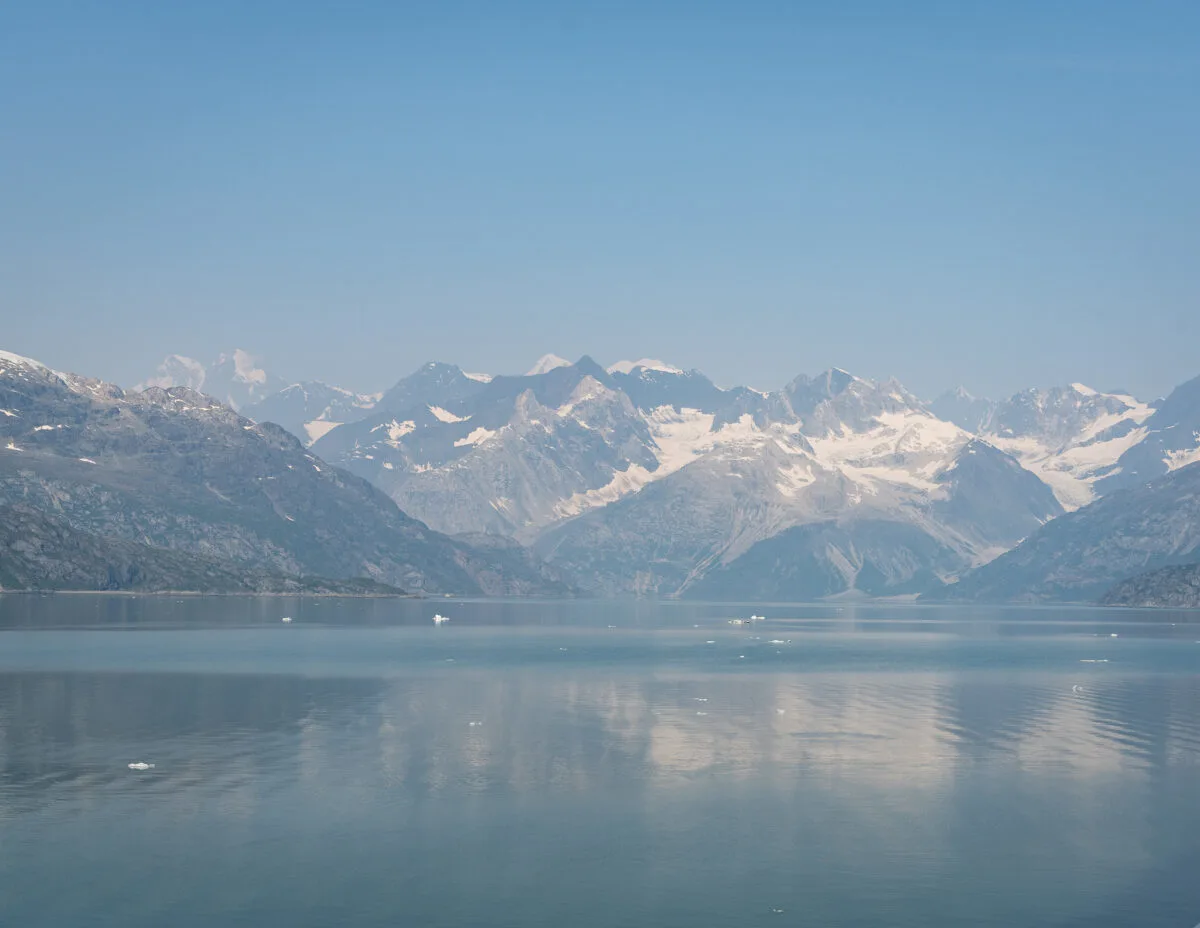 snow colored mountains reflected against the the bay with chunks of glaciers in the water
