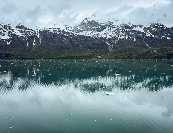 Early morning views while cruising Glacier Bay National Park in Alaska, with snow-covered mountains reflecting on calm water dotted with small floating ice.
