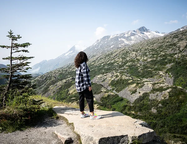 kathy standing against the mountain backdrop of where the welcome to alaska sign is located