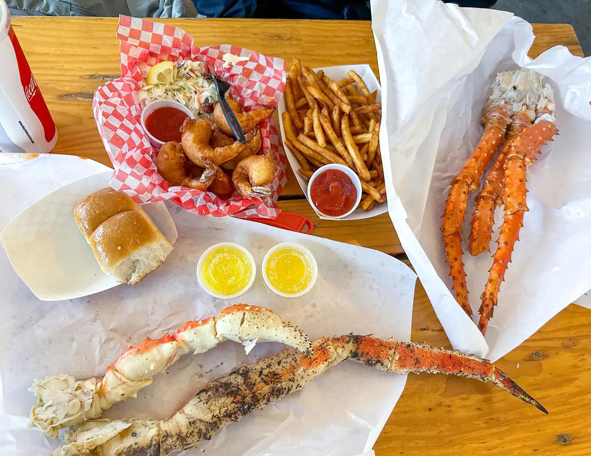 A table spread with Alaskan seafood at Tracy’s King Crab Shack, featuring king crab legs, beer-battered shrimp, fries, and dipping sauces.