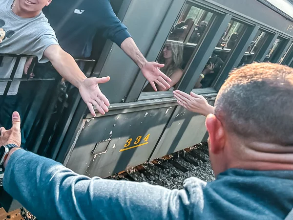 Passengers from two passing trains reaching out for a high-five, emphasizing a moment of connection amidst travel.