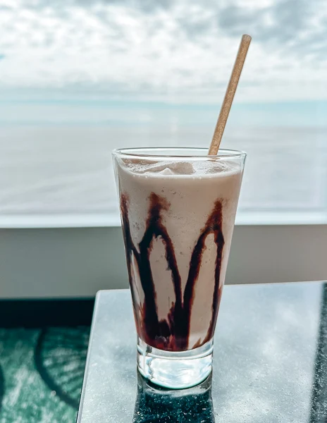 mudsline drink with a straw sitting on a table with a view of the ocean in the background
