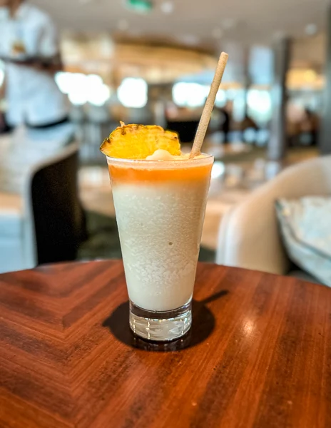 pina colada served in a glass with a slice of pineapple, liquor floating on top, sitting on top of a table