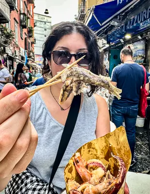 kathy holding up fried sardines to the camera while eating fried seafood in naples italy