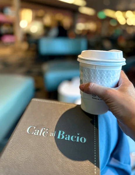 holding a cup of coffee and cafe al bacio menu on celebrity beyond