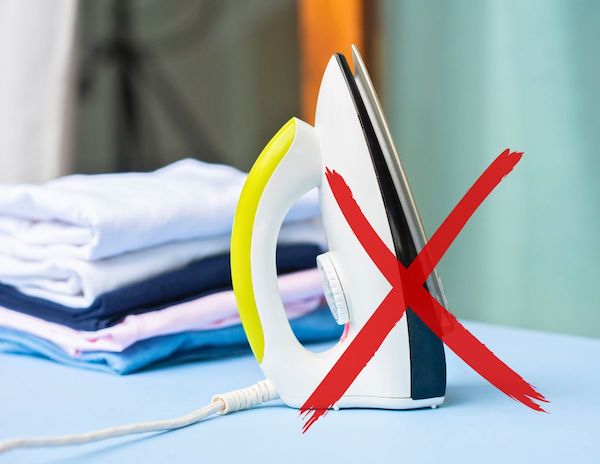 red x over an iron sitting on a table with folded clothes next to it