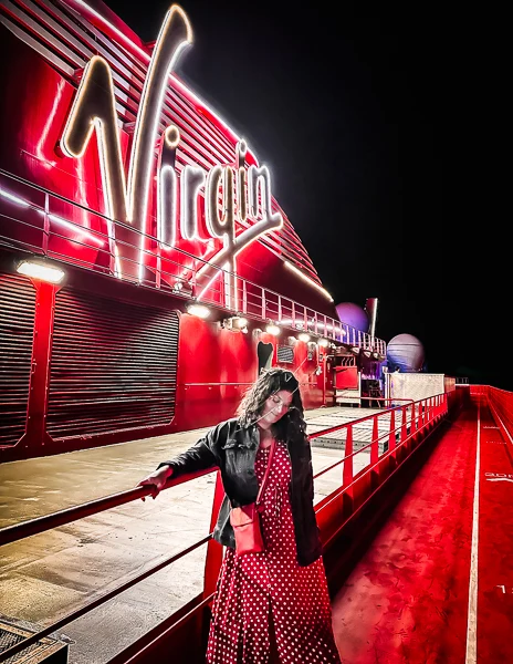 kathy standing by the virgin sign glowing at night on the cruise ship