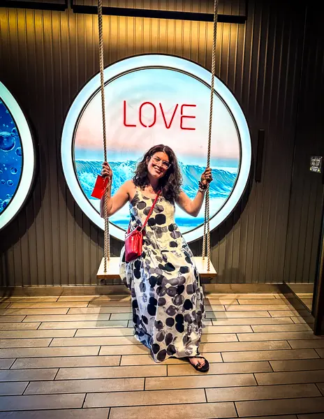 kathy siting on a swing seat in front of a Love sign on scarlet lady