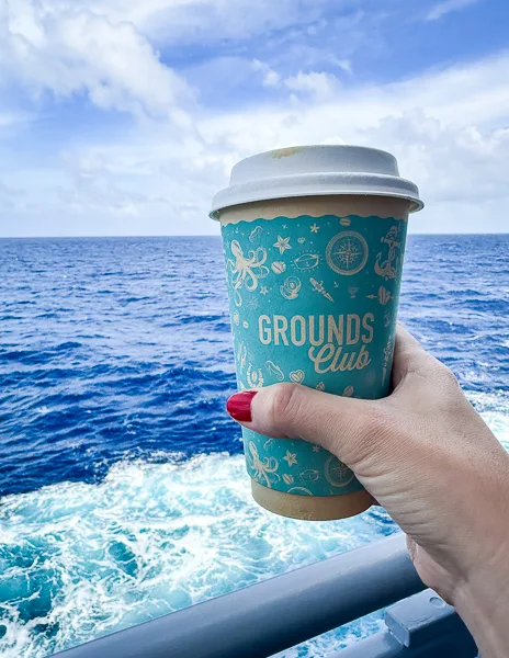 holding a cup of coffee from the grounds club with the view of the ocean