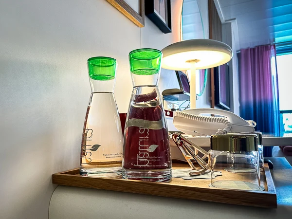 two pitchers of water and glasses set on a tray by a light fixture vanity in the sea terrace cabin of virign voyages