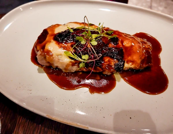 A plate of Bistec Marinero en Escabeche from Pink Agave onboard Virgin Voyages, featuring a marinated steak topped with herbs.