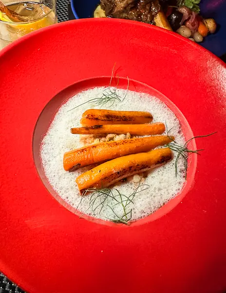 A vibrant presentation of carrots in brown butter from Razzle Dazzle on Virgin Voyages, served in a bright red bowl.