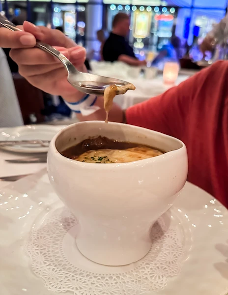 a spoonful of French Onion Soup being lifted from a classic white soup bowl at le bistro on ncl breakaway