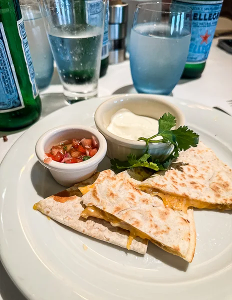 A chicken cheese quesadilla served with sour cream and a small bowl of salsa.