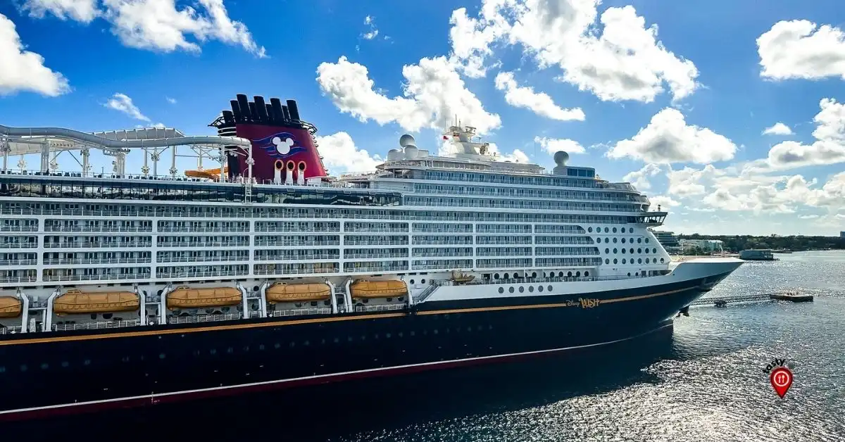 Disney Wish cruise ship docked under a sunny blue sky, showcasing its sleek design, multiple decks, and signature Disney Cruise Line red funnel with Mickey Mouse accents