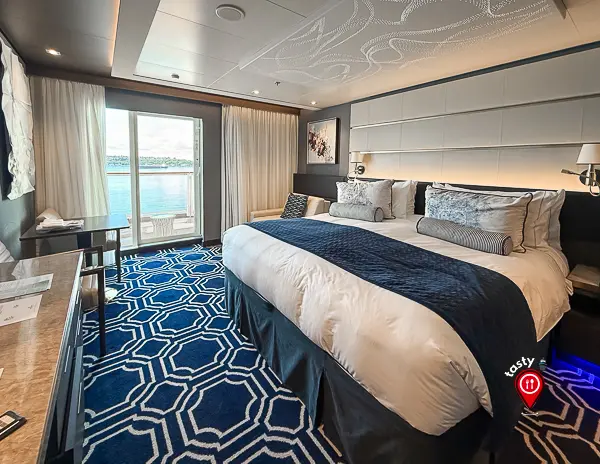 Spacious NCL Haven Penthouse Suite aboard the Norwegian Encore, featuring a king-sized bed, modern decor, and balcony views overlooking the ocean.
