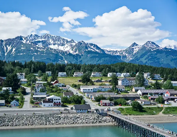 View of Haines, Alaska, from the cruise port with snow-covered mountains and small-town buildings under a blue sky.