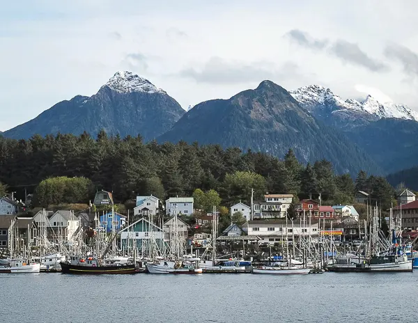 View of Sitka, Alaska, with fishing boats docked in the harbor and snow-capped mountains in the background.