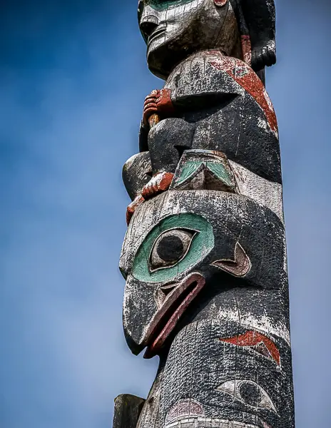Close-up of a carved and painted totem pole in Sitka, Alaska, against a blue sky.