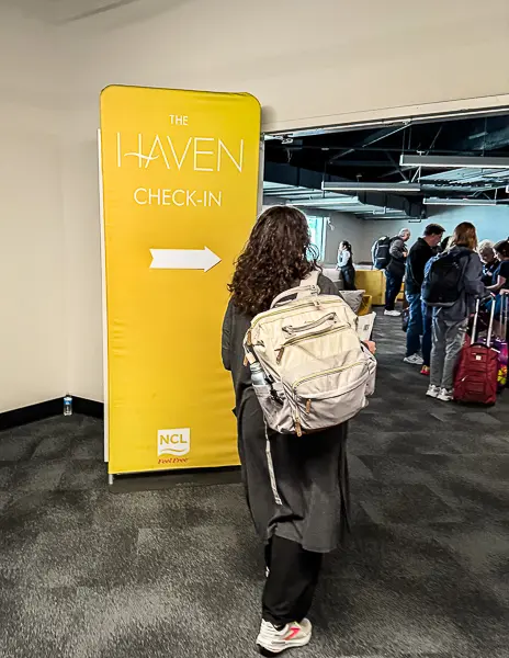 Passenger walking toward The Haven check-in area at the Seattle cruise terminal with a yellow NCL sign indicating priority embarkation for Haven guests