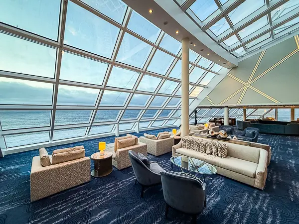 Spacious seating area inside The Haven Observation Lounge on Norwegian Encore with floor-to-ceiling windows offering panoramic ocean views