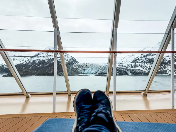 Relaxing on The Haven Sundeck aboard Norwegian Encore with a view of Lamplugh Glacier in Glacier Bay, Alaska through floor-to-ceiling windows