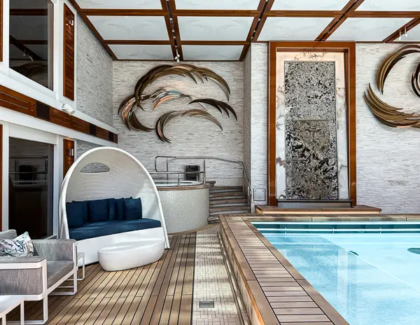 Hidden hot tub behind curved lounge seating in The Haven Courtyard on Norwegian Encore, with modern art and a waterfall feature nearby