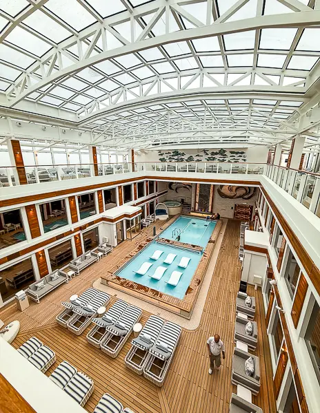 Full view of The Haven Courtyard on Norwegian Encore, with retractable glass roof, loungers, pool, hot tub, and two-story suite balconies
