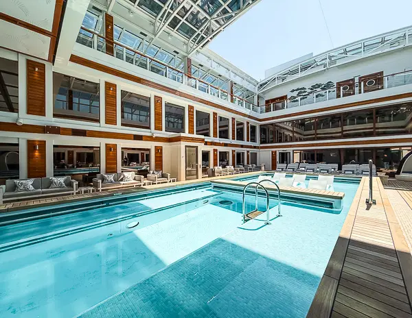 The Haven Courtyard on Norwegian Encore, showing the private pool, lounge chairs, and two-story suite balconies under a retractable roof