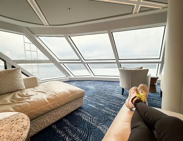 Lounging in The Haven Observation Lounge on Norwegian Encore with feet up on a chaise, enjoying the ocean view while cruising Alaska