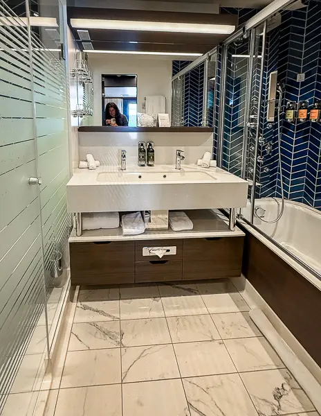 Full bathroom of NCL Encore Haven Penthouse Suite 17112 with double sink, walk-in shower, and bathtub.