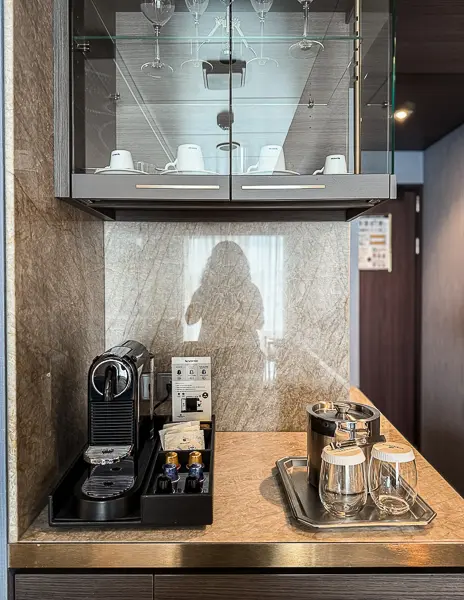 Coffee and glassware station inside Norwegian Encore Haven Penthouse Suite 17112, featuring a Nespresso machine, cups, glasses, and a mirrored backsplash.