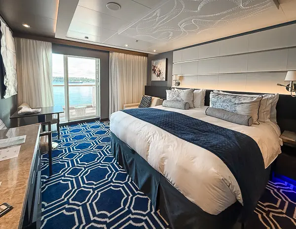 Norwegian Encore Haven Penthouse Suite 17112 with king-size bed and view of the extended balcony through the glass doors.
