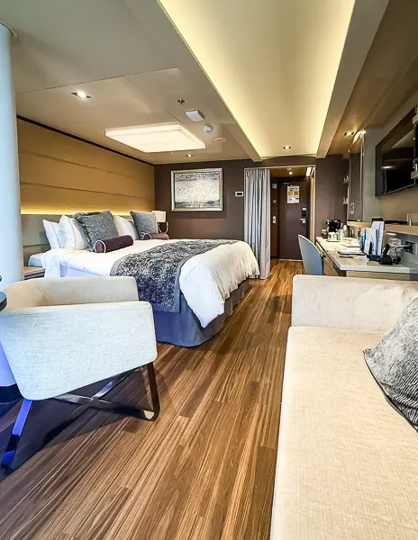 Full view of Haven Suite 14138 on Norwegian Getaway showing the bed, sofa, vanity area with coffee station, and partial view of the column near the jacuzzi.