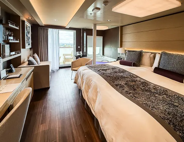 Norwegian Getaway’s Haven Suite 14138 with king bed, sofa, and corner jacuzzi tub near the balcony.