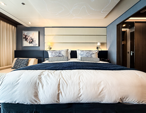 King-size bed in Norwegian Encore Haven Penthouse Suite 17112, with closet area visible to the right.