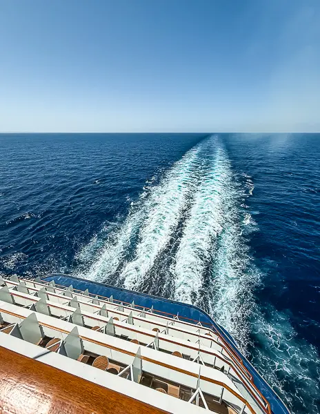 Wake from the back of a cruise ship on a sea day showing calm blue water and clear skies, debunking the myth of giant waves at sea.