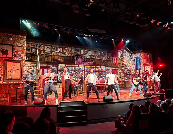 Cast of The Choir of Man performing on stage aboard the Norwegian Encore, with a vibrant pub-style set and colorful lighting.