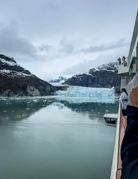 Cruise passengers observing a massive tidewater glacier from the deck while sailing through Glacier Bay, Alaska, surrounded by icy waters and rugged peaks.