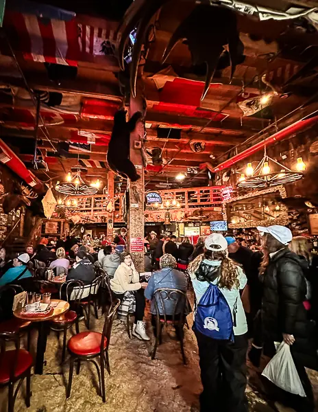 Crowd of visitors inside the lively Red Dog Saloon in Juneau, Alaska, with eclectic decor, mounted wildlife, and flags hanging from the ceiling.