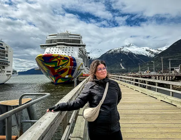 Standing on the dock in Skagway, Alaska, with the Norwegian Encore cruise ship and snow-capped mountains in the background