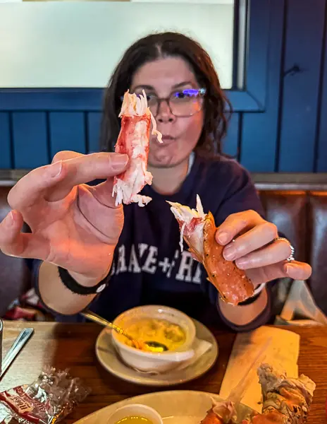 Woman (kathy) holding up freshly cracked crab leg meat at The Hangar restaurant in Juneau, Alaska, with a bowl of dipping butter and salmon chowder on the table.