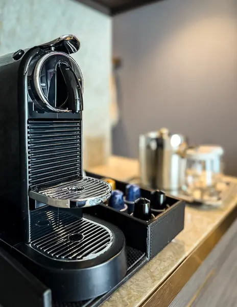 Nespresso machine setup inside our Haven Penthouse suite on the Norwegian Encore, with coffee pods, an ice bucket, and glassware nearby.