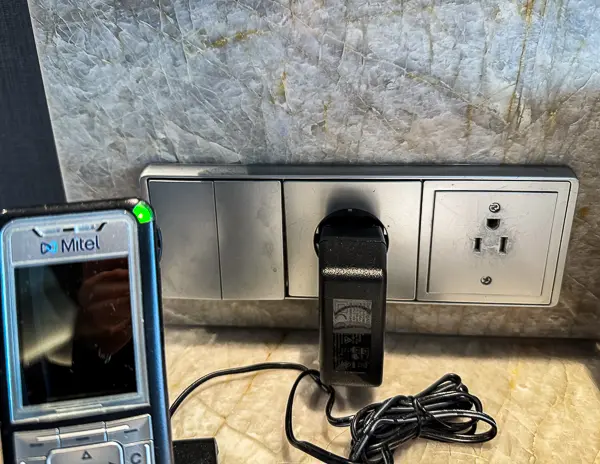 Electrical outlets and European plug setup in the Haven Penthouse suite on the Norwegian Encore, with a cordless phone plugged in.