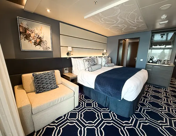 King bed and sitting area inside the Haven Penthouse Suite on the Norwegian Encore Cabin 17112, showing the room’s modern decor and built-in espresso station.