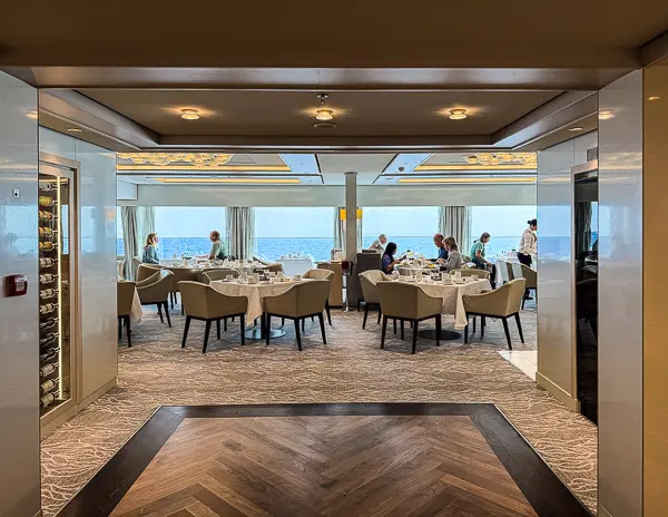Interior of the Haven Restaurant on Norwegian Encore, with white tablecloths, ocean views, and guests dining in a bright, elegant setting