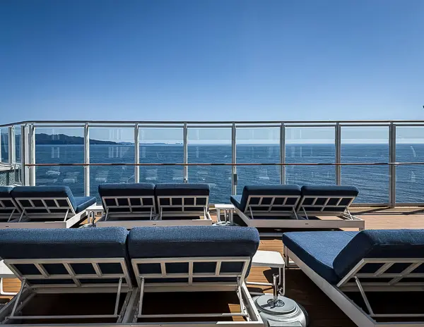 Ocean-facing loungers on The Haven sundeck aboard Norwegian Encore with clear views of the sea and coastline on a sunny day