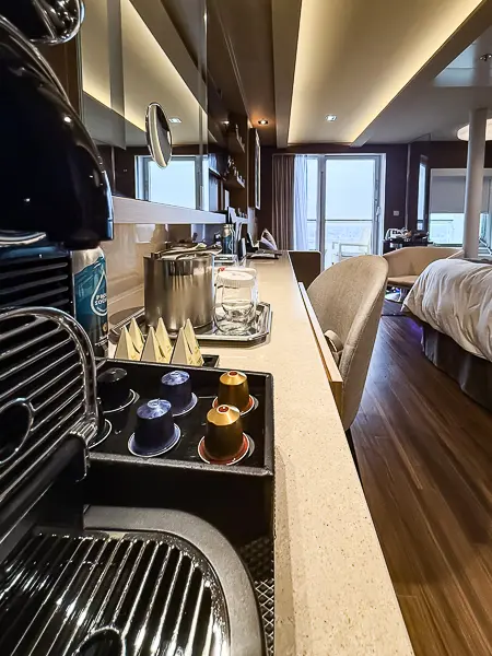 Sitting area of Haven Suite 14138 on Norwegian Getaway with sofa, armchair, and small table near the balcony and corner jacuzzi tub.