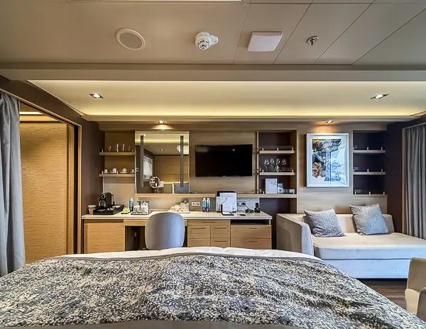 View of the king bed, vanity area, and coffee station inside The Haven Suite 14138 on Norwegian Getaway.